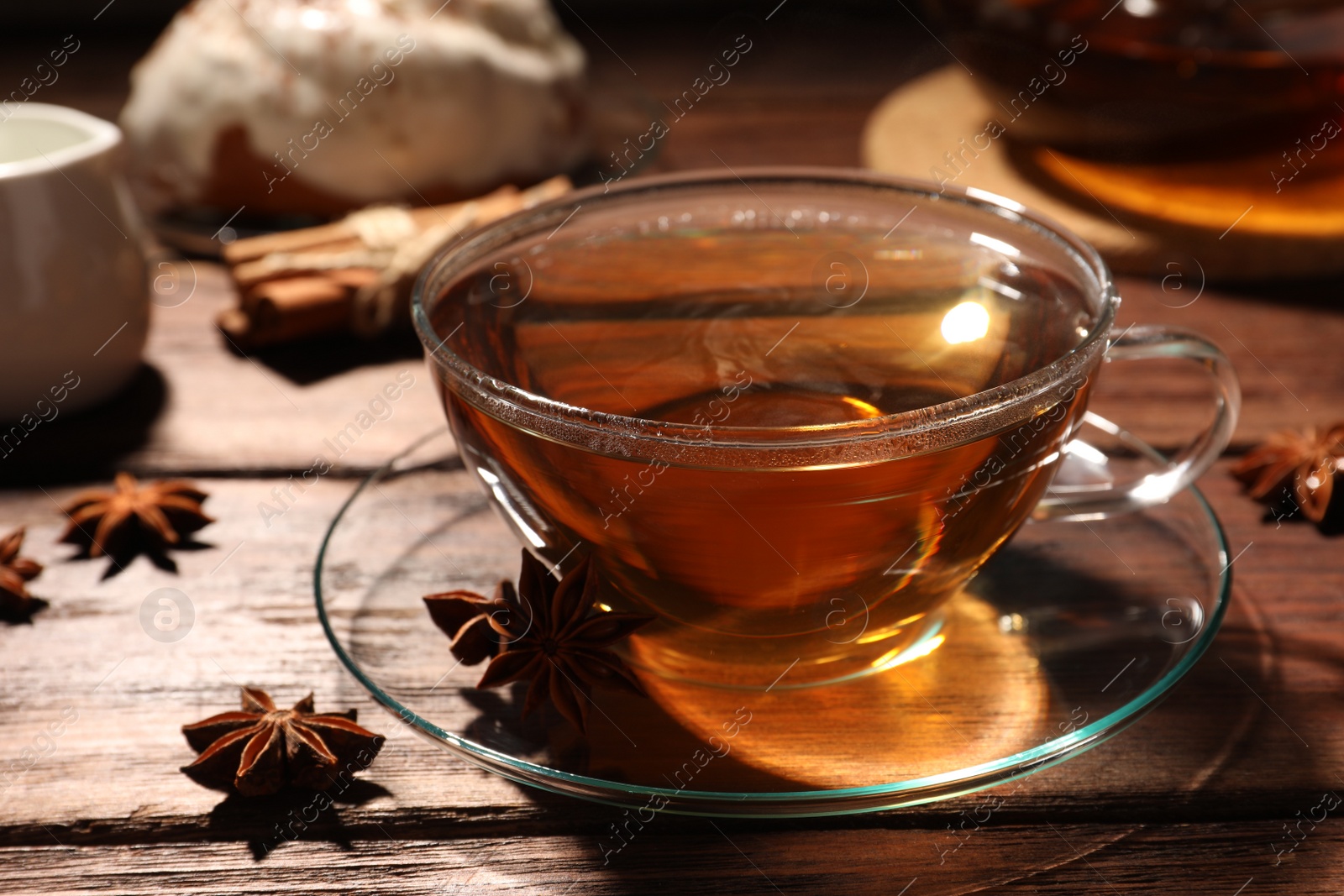 Photo of Glass cup of aromatic hot tea with anise stars on wooden table