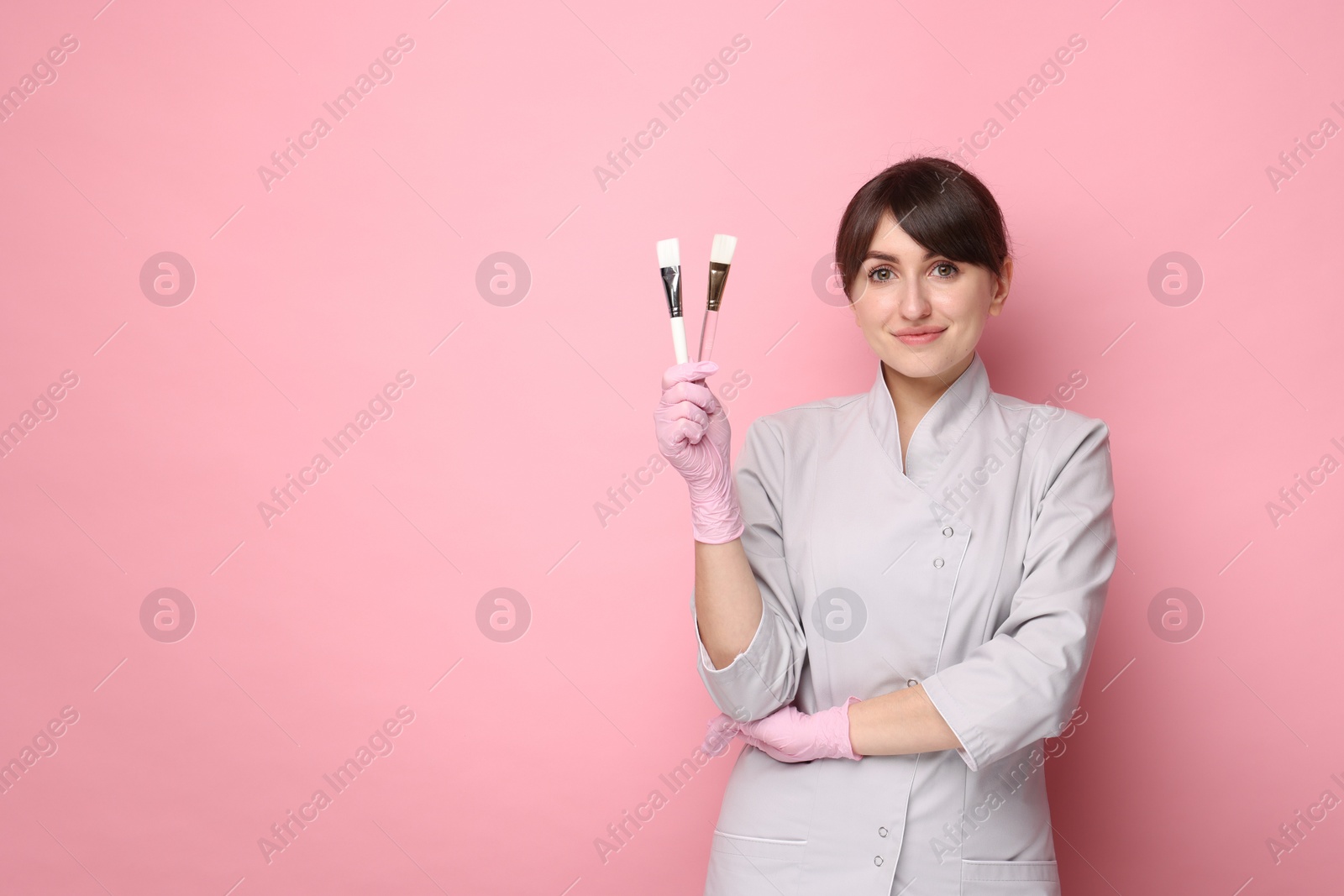 Photo of Cosmetologist with cosmetic brushes on pink background, space for text