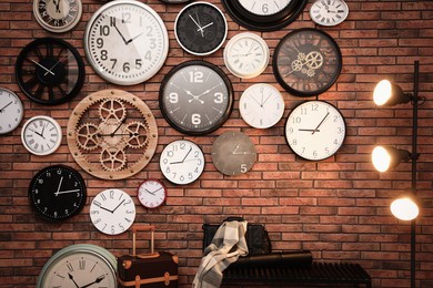 Photo of Collection of clocks hanging on red brick wall indoors