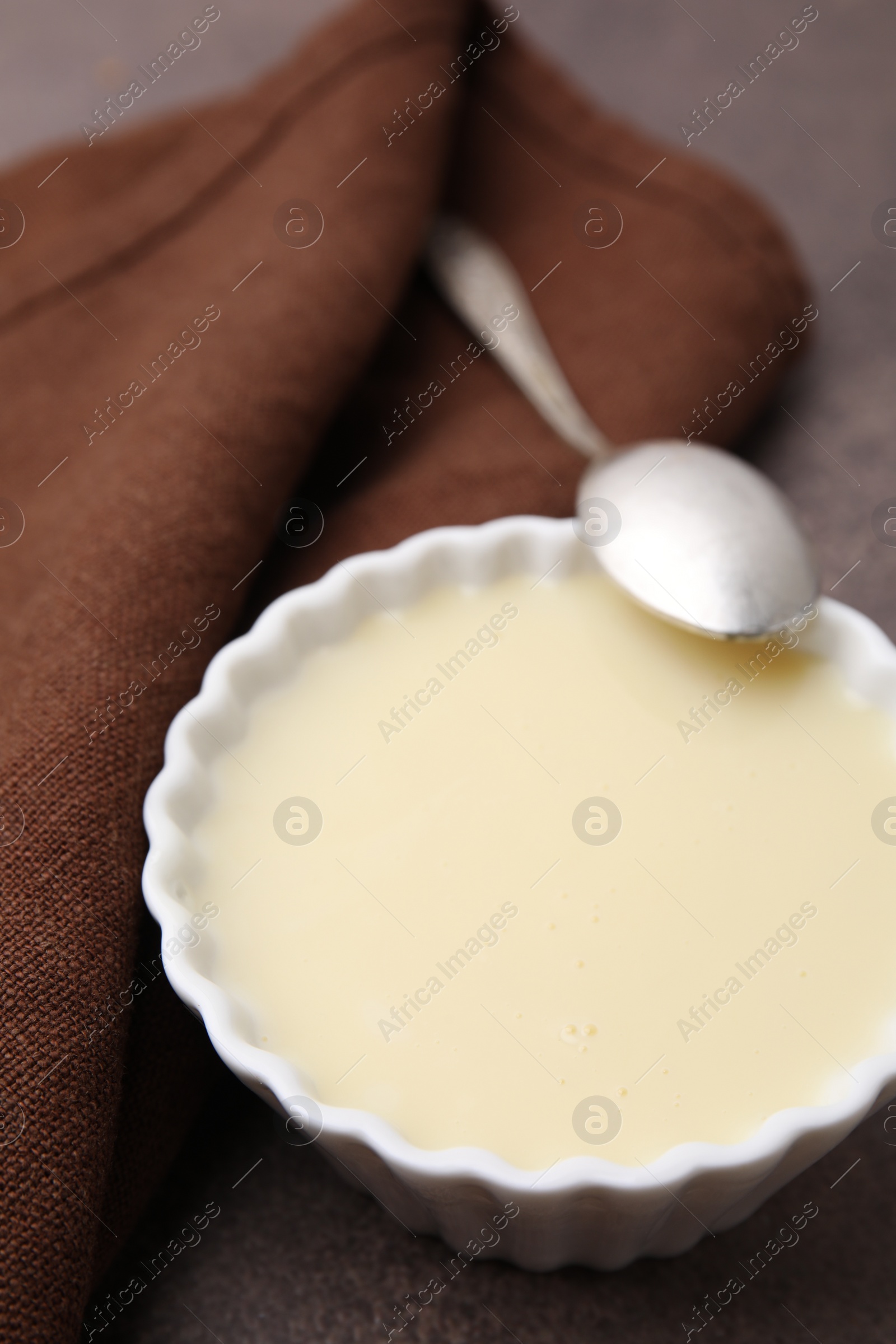 Photo of Bowl with condensed milk and spoon on brown table, closeup