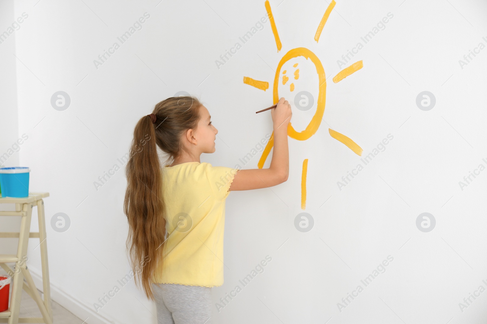 Photo of Little child painting sun on white wall indoors