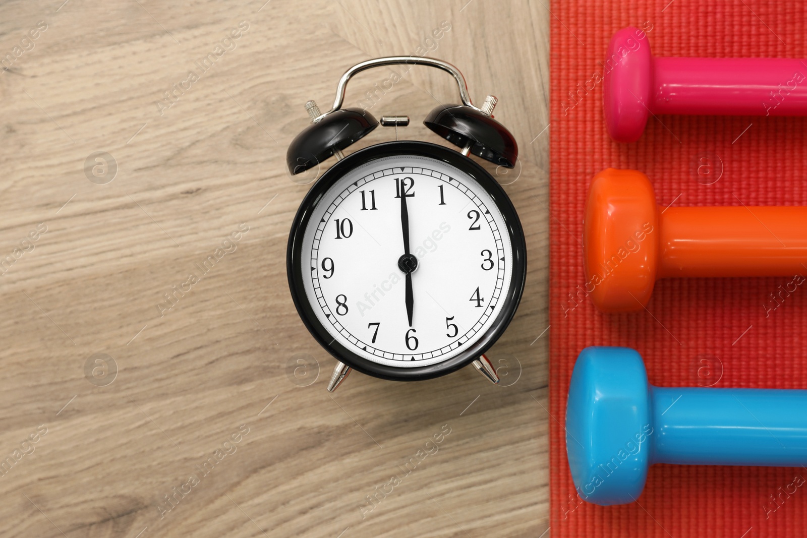 Photo of Alarm clock, yoga mat and dumbbells on wooden background, flat lay. Morning exercise