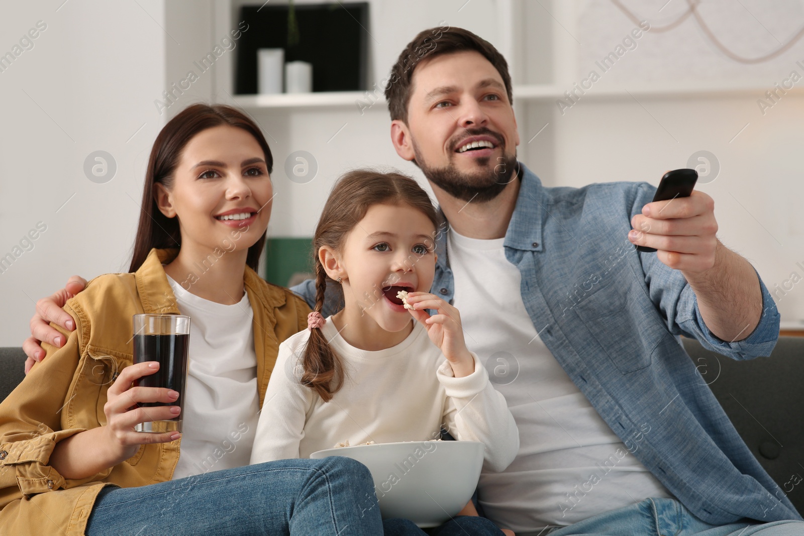 Photo of Happy family watching movie at home. Father changing TV channels with remote control