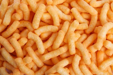 Photo of Many tasty cheesy corn puffs as background, top view