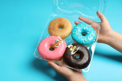 Photo of Woman with box of delicious donuts on light blue background, closeup