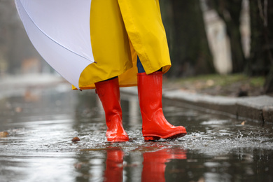 Photo of Woman in rubber boots with umbrella walking outdoors on rainy day, closeup