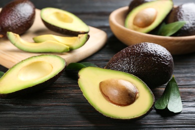 Whole and cut avocados with green leaves on dark wooden table, closeup