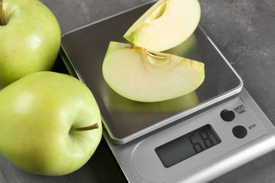 Photo of Kitchen scale with pieces of apple and fruits on grey textured table, closeup