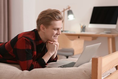 Online learning. Smiling teenage boy with laptop on bed at home