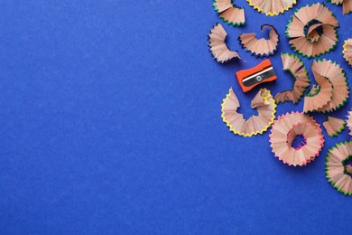 Photo of Colorful pencil shavings and sharpener on blue background, flat lay. Space for text