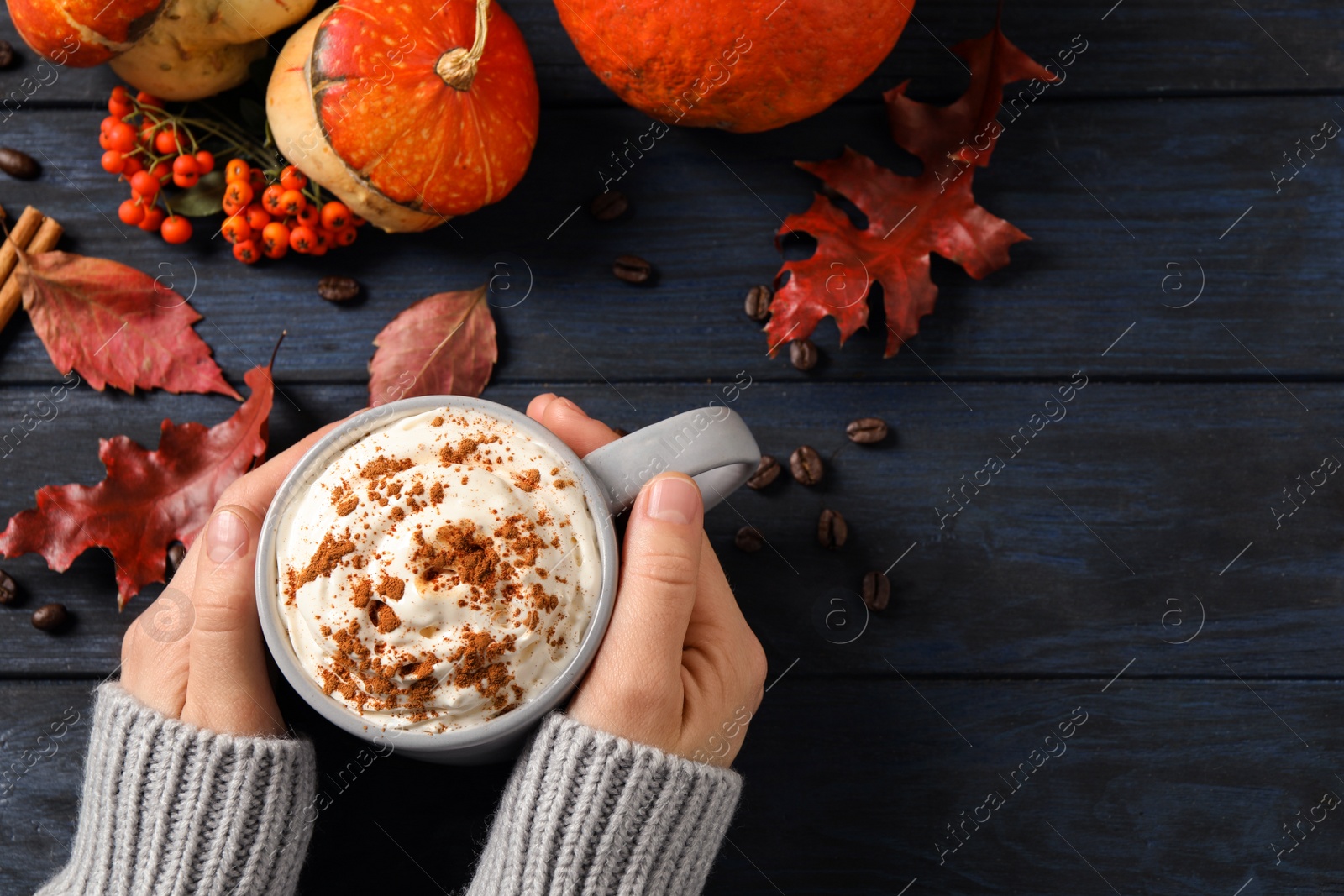 Photo of Woman with cup of tasty pumpkin spice latte at wooden table, top view. Space for text