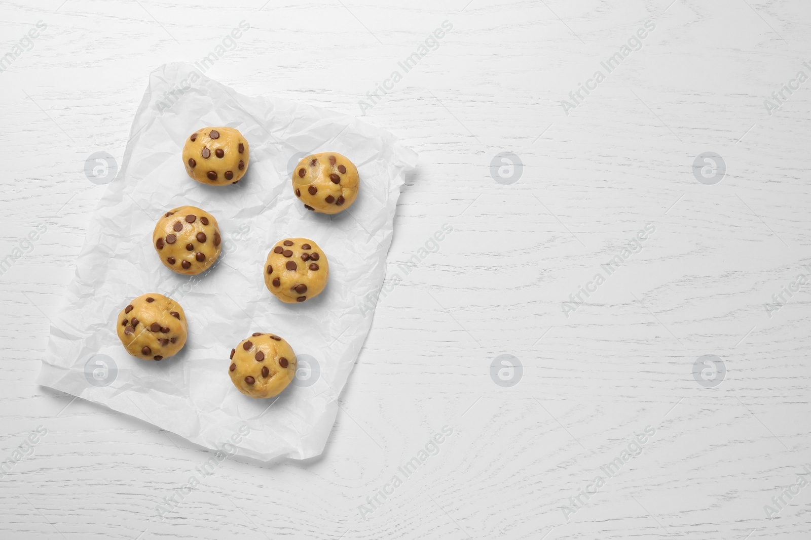 Photo of Uncooked chocolate chip cookies on white wooden table, top view. Space for text