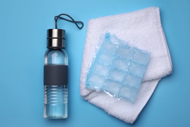Photo of Bottle of water, ice pack and towel on light blue background, flat lay. Heat stroke treatment