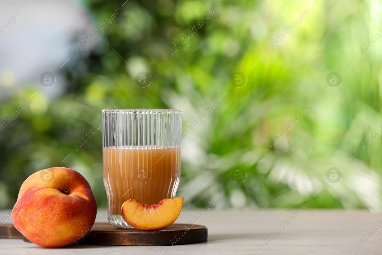 Photo of Glass of tasty peach juice and fresh fruits on white table outdoors, space for text