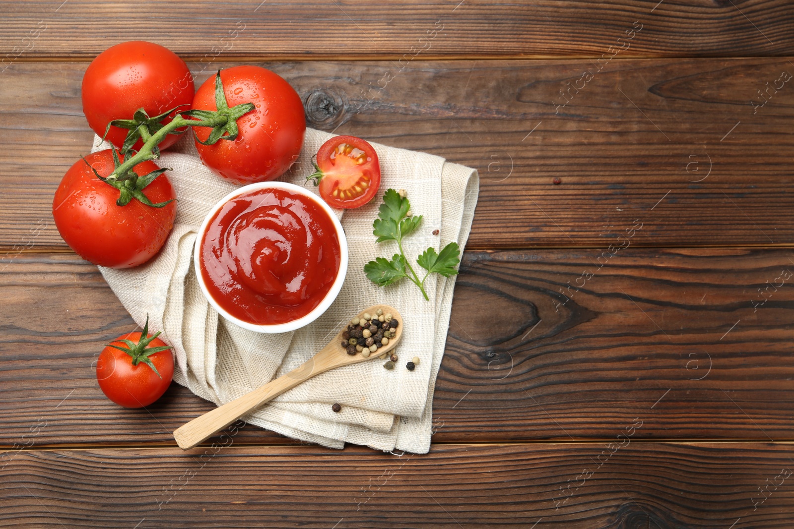 Photo of Delicious ketchup in bowl, tomatoes, parsley and peppercorns on wooden table, top view. Space for text