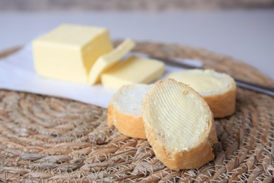 Photo of Tasty cut baguette with fresh butter on wicker mat, closeup