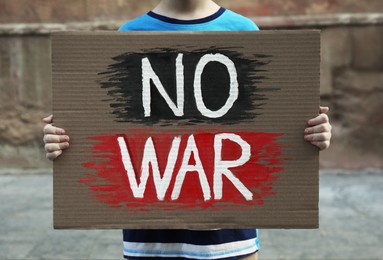 Photo of Boy holding poster with words No War outdoors, closeup