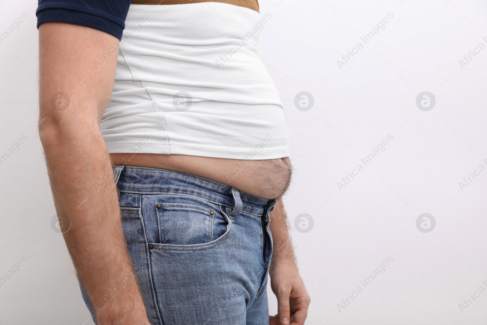 Photo of Man wearing tight t-shirt and jeans on white background, closeup. Overweight problem