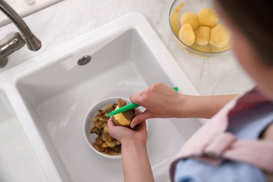 Woman peeling potato near kitchen sink, closeup. Preparing vegetable