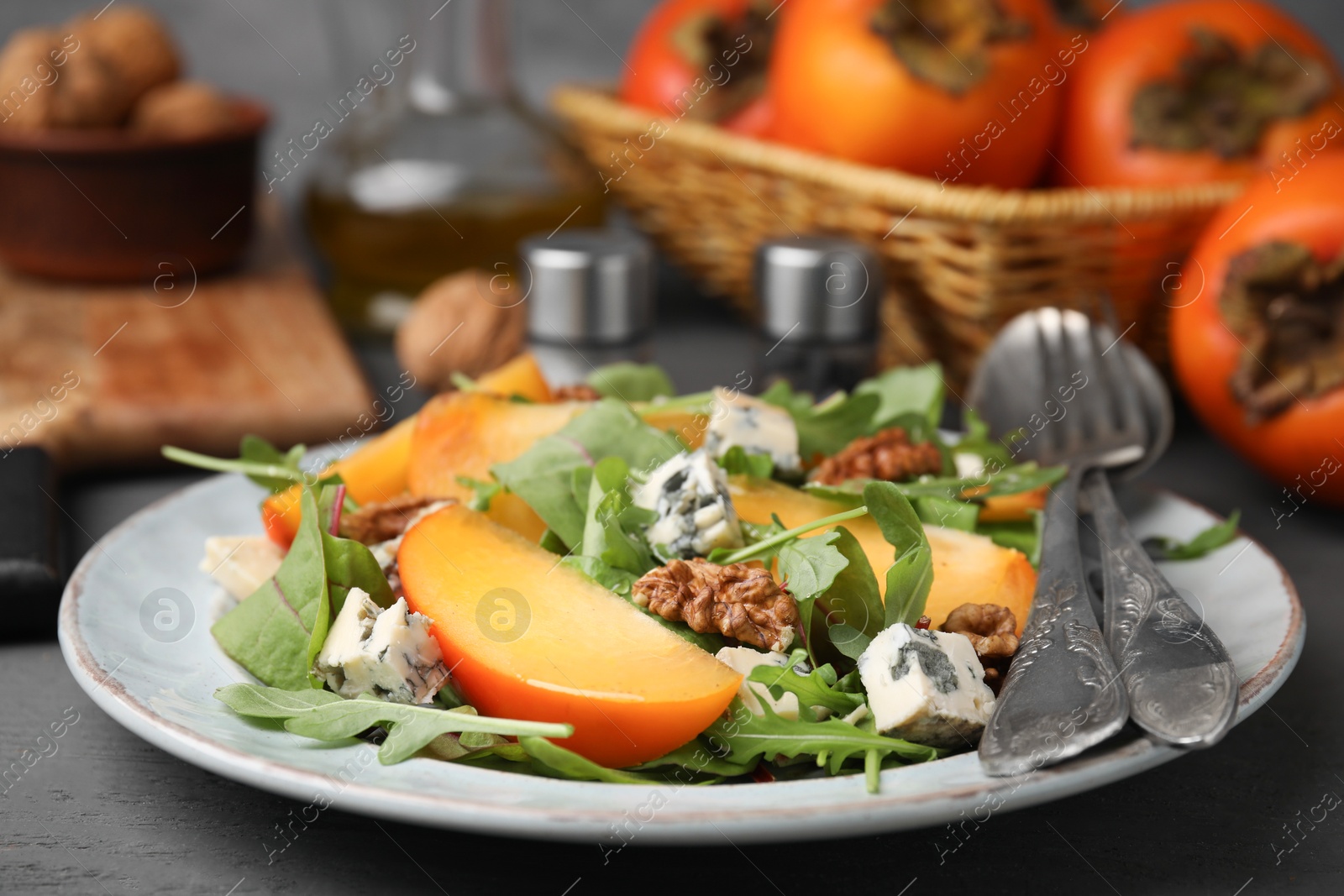 Photo of Tasty salad with persimmon, blue cheese and walnuts served on grey wooden table, closeup