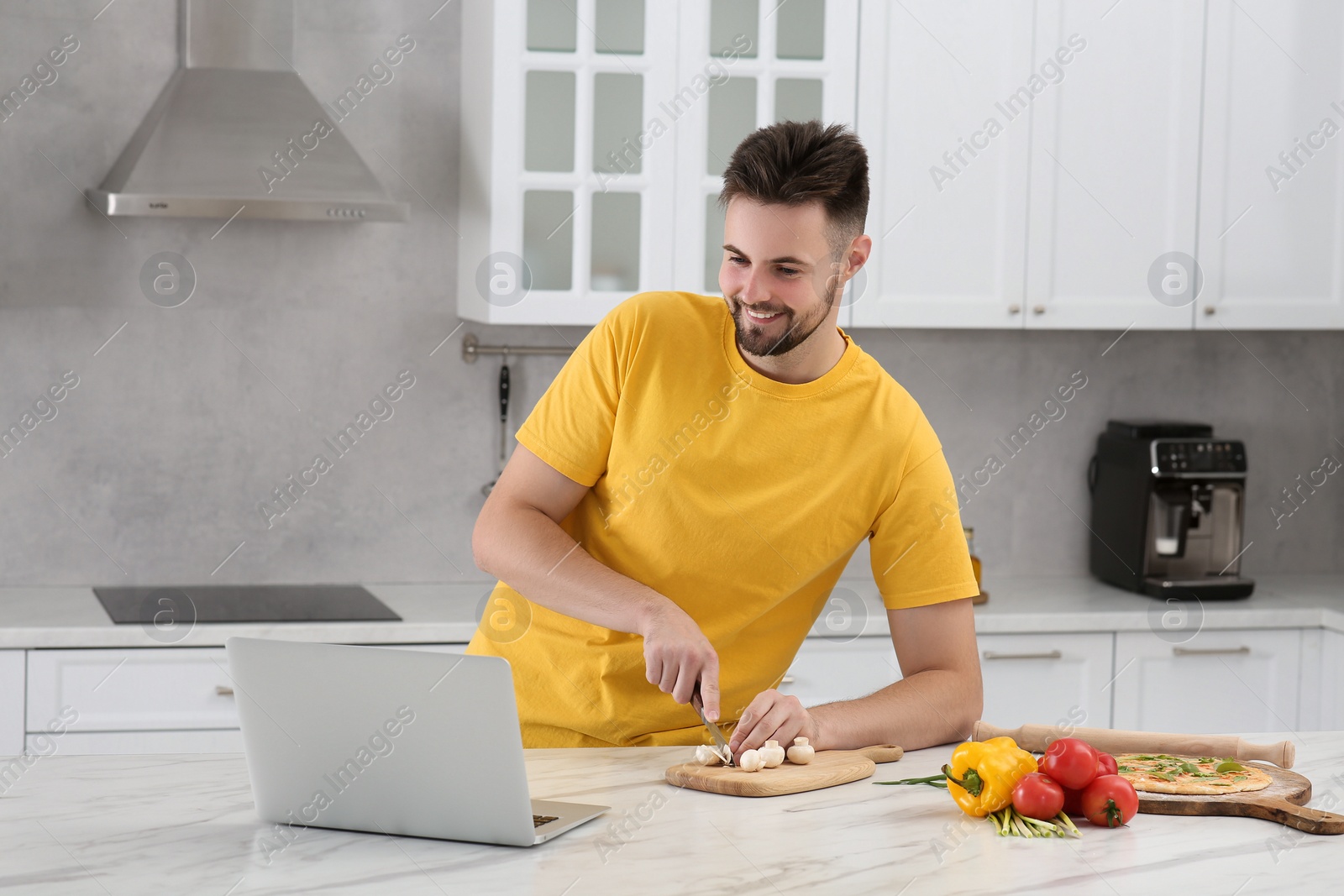 Photo of Man watching cooking online course on laptop while cutting mushrooms in kitchen. Time for hobby