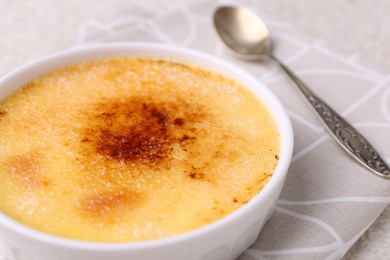 Photo of Delicious creme brulee in bowl and spoon on table, closeup