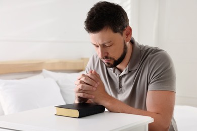 Photo of Religious man with Bible praying in bedroom