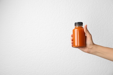 Photo of Woman holding bottle of carrot juice on grey background, closeup with space for text