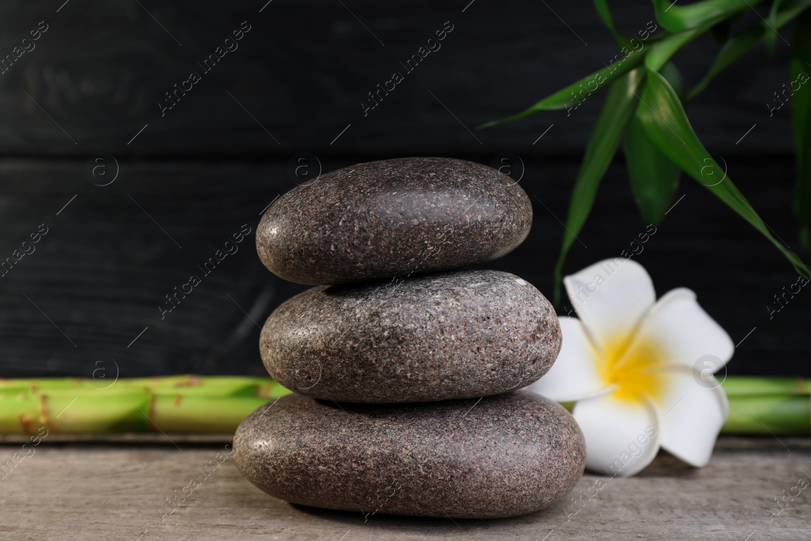 Photo of Stacked spa stones, bamboo and flower on wooden table