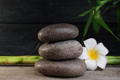 Photo of Stacked spa stones, bamboo and flower on wooden table