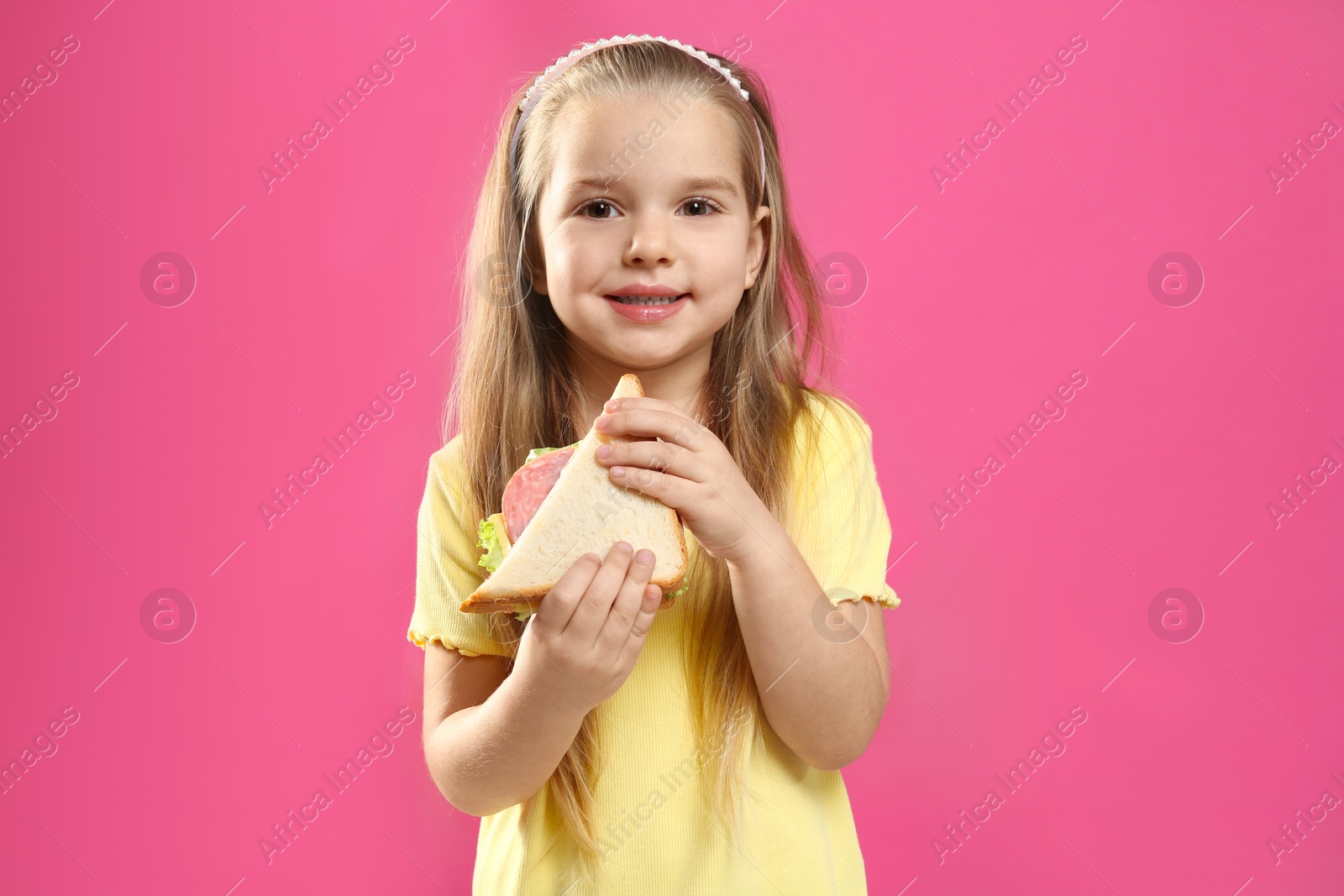 Photo of Cute little girl with tasty sandwich on pink background