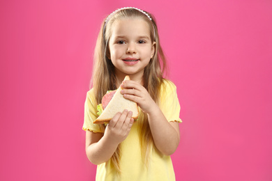 Cute little girl with tasty sandwich on pink background