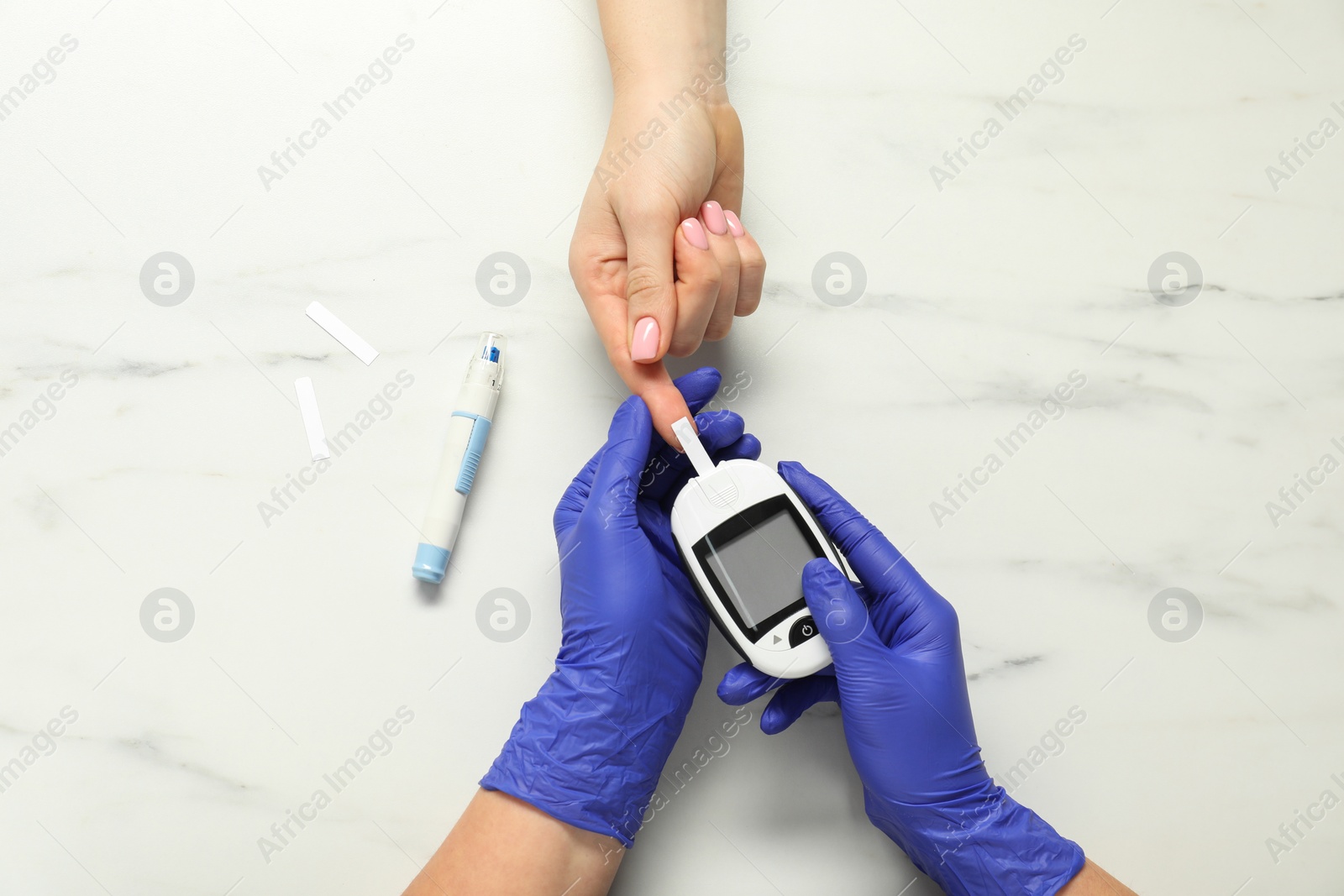Photo of Diabetes. Doctor checking patient's blood sugar level with glucometer at white marble table, top view