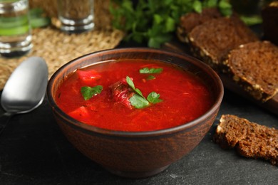 Photo of Stylish brown clay bowl with Ukrainian borsch on black table