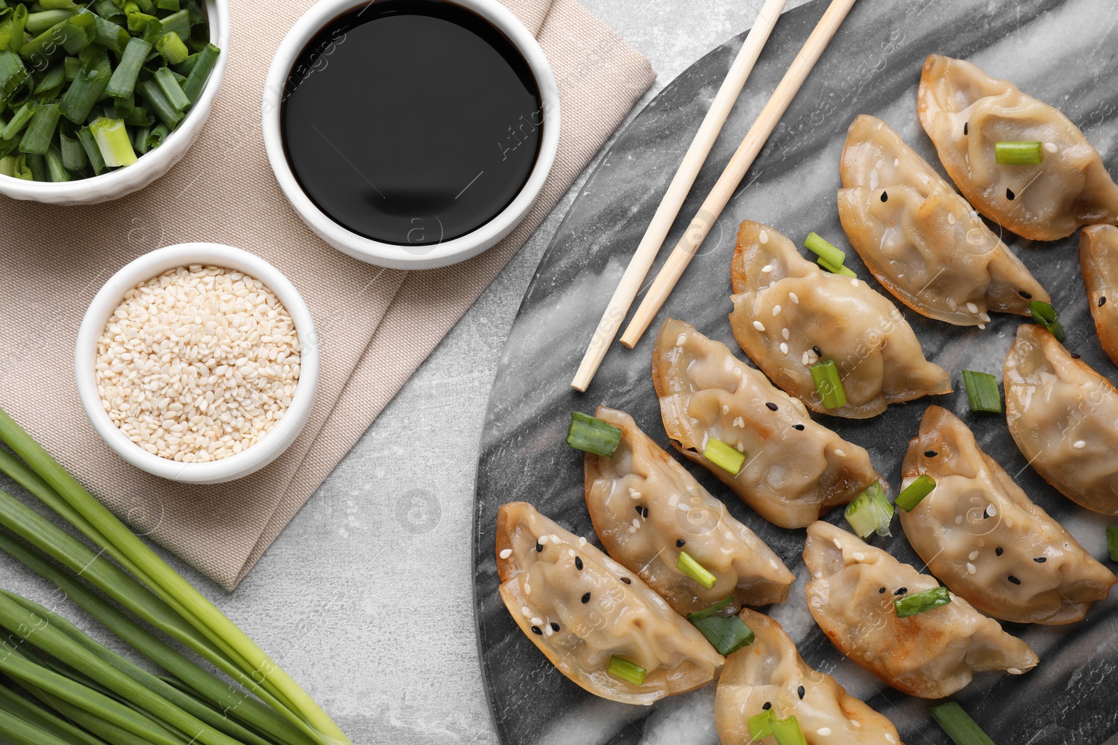 Photo of Delicious gyoza (asian dumplings) with green onions, sesame, soy sauce and chopsticks on light gray table, flat lay