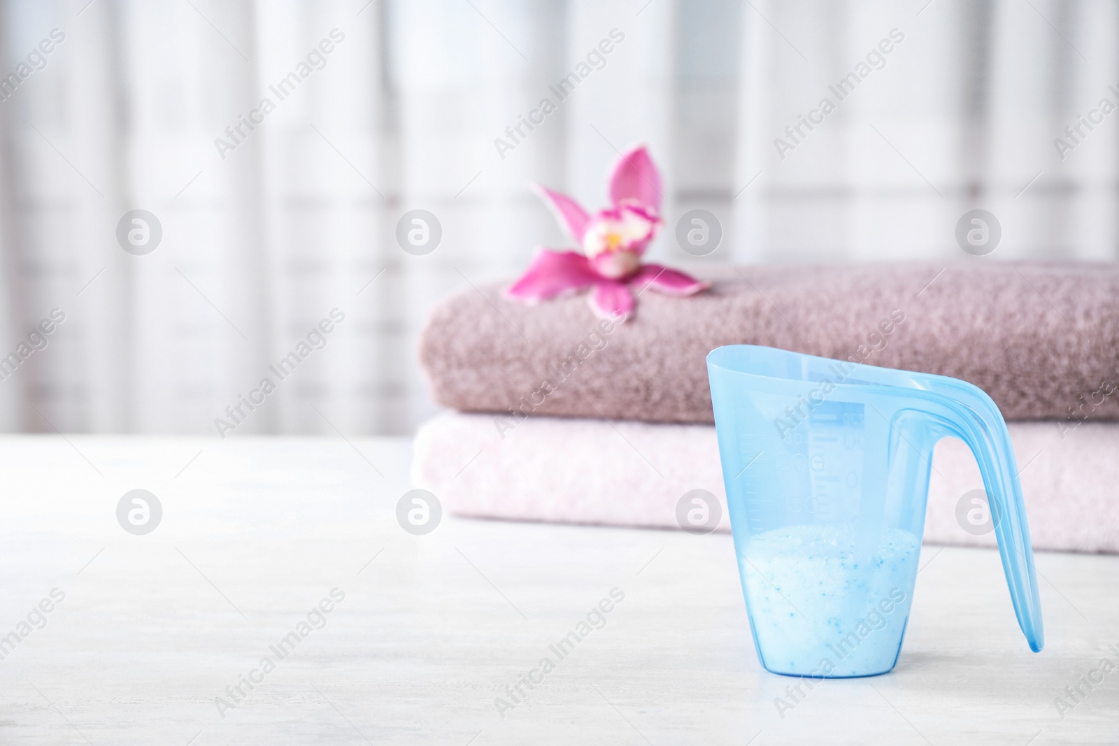 Photo of Measuring cup of washing powder on table against blurred background. Space for text