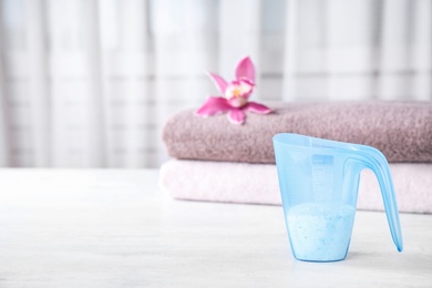 Photo of Measuring cup of washing powder on table against blurred background. Space for text