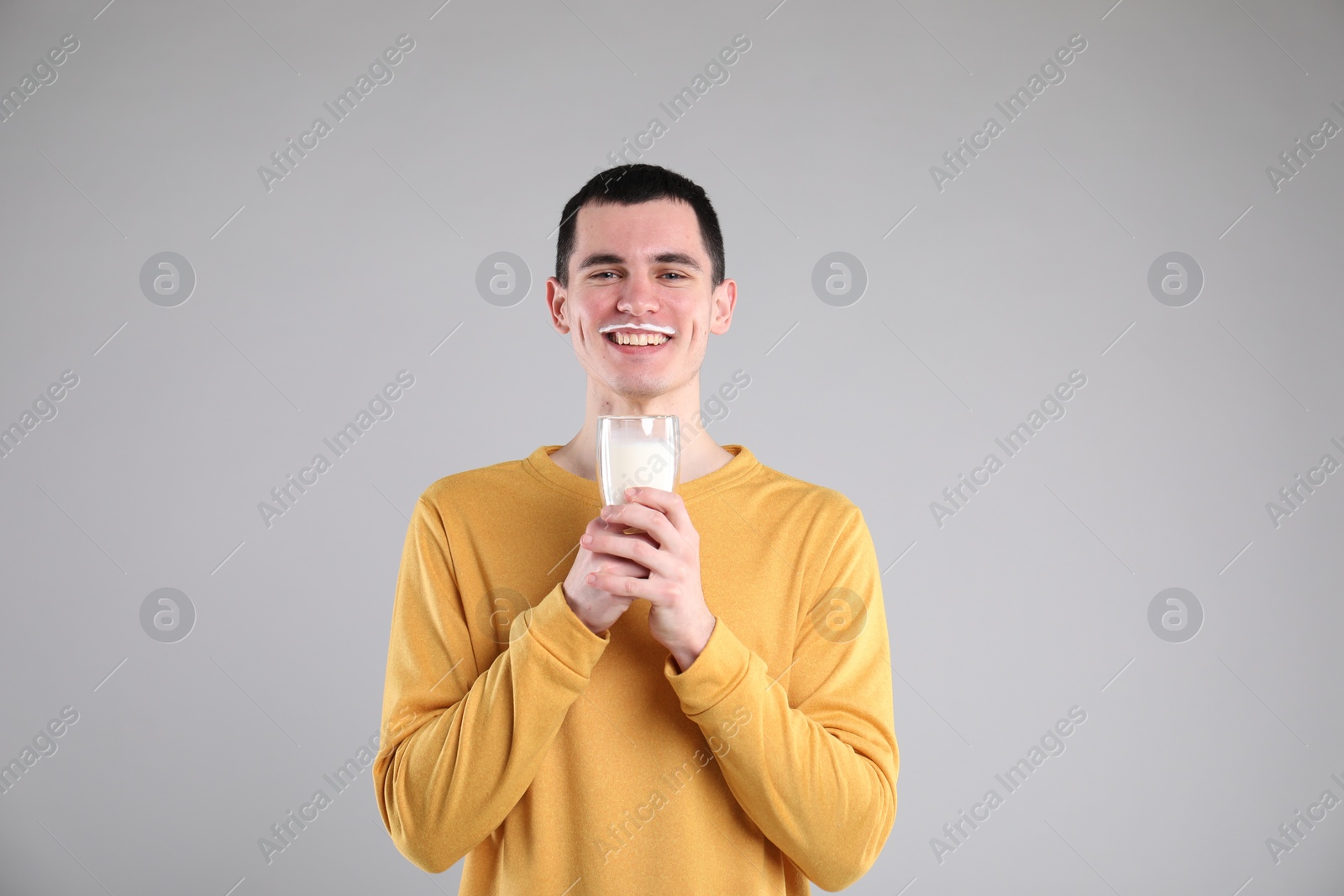 Photo of Happy man with milk mustache holding glass of tasty dairy drink on gray background