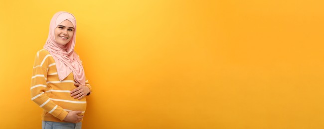 Image of Portrait of pregnant Muslim woman in hijab on yellow background, space for text. Banner design