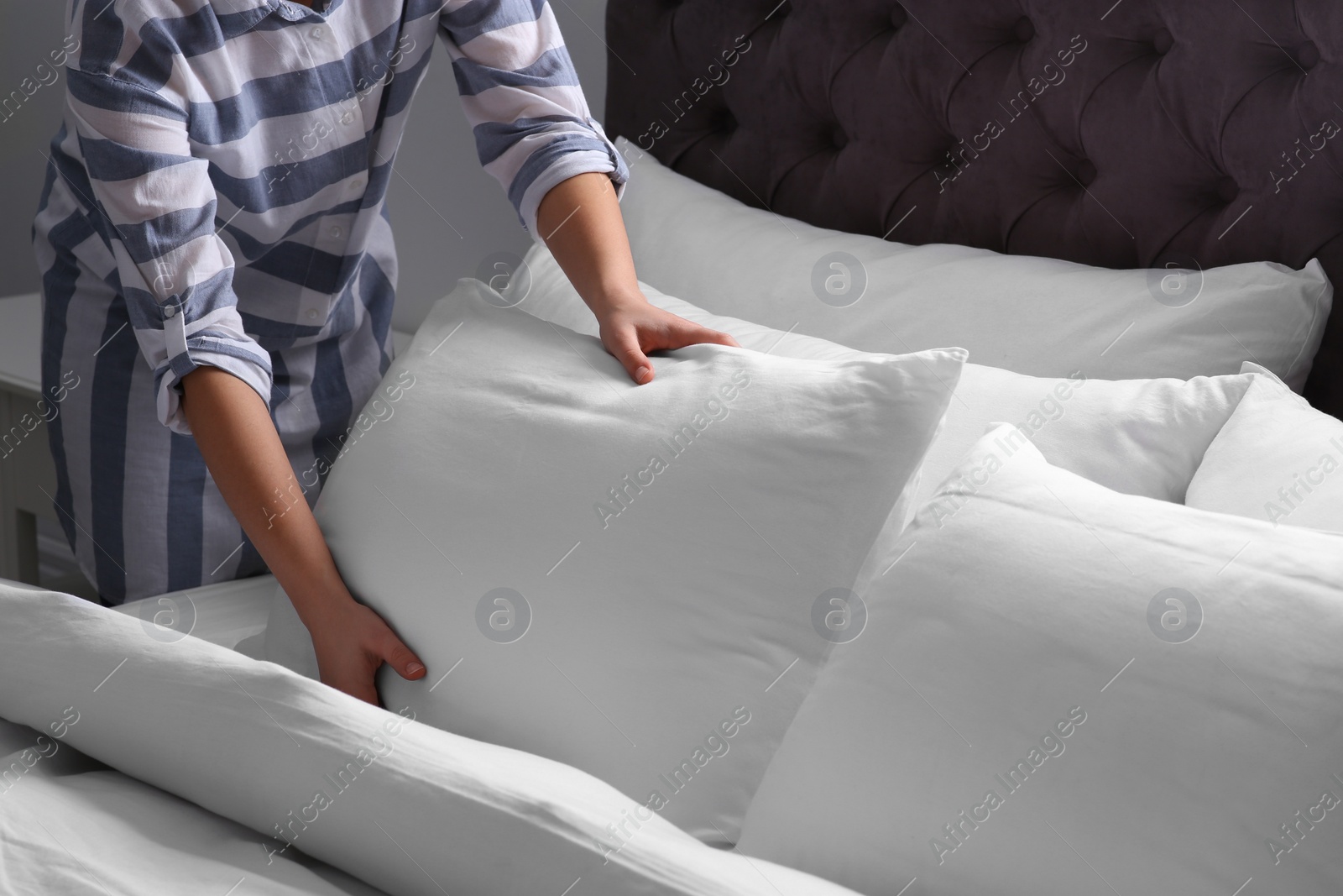 Photo of Woman fluffing white pillow on bed, closeup