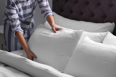 Photo of Woman fluffing white pillow on bed, closeup