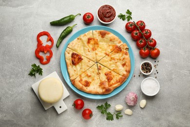 Delicious khachapuri with cheese surrounded by different products on grey table, flat lay