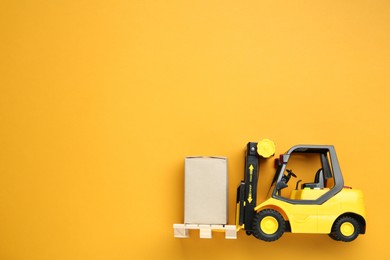 Photo of Toy forklift with wooden pallet and box on orange background, top view. Space for text