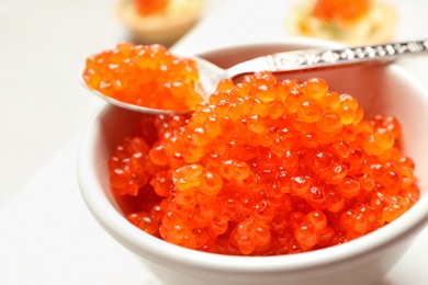 Photo of Spoon and bowl with delicious red caviar on light background, closeup