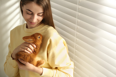 Photo of Young woman with adorable rabbit indoors. Lovely pet