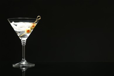 Photo of Martini cocktail with ice and olives on dark background. Space for text