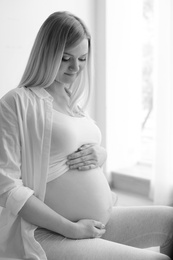 Photo of Beautiful pregnant woman sitting in light room at home, black and white effect