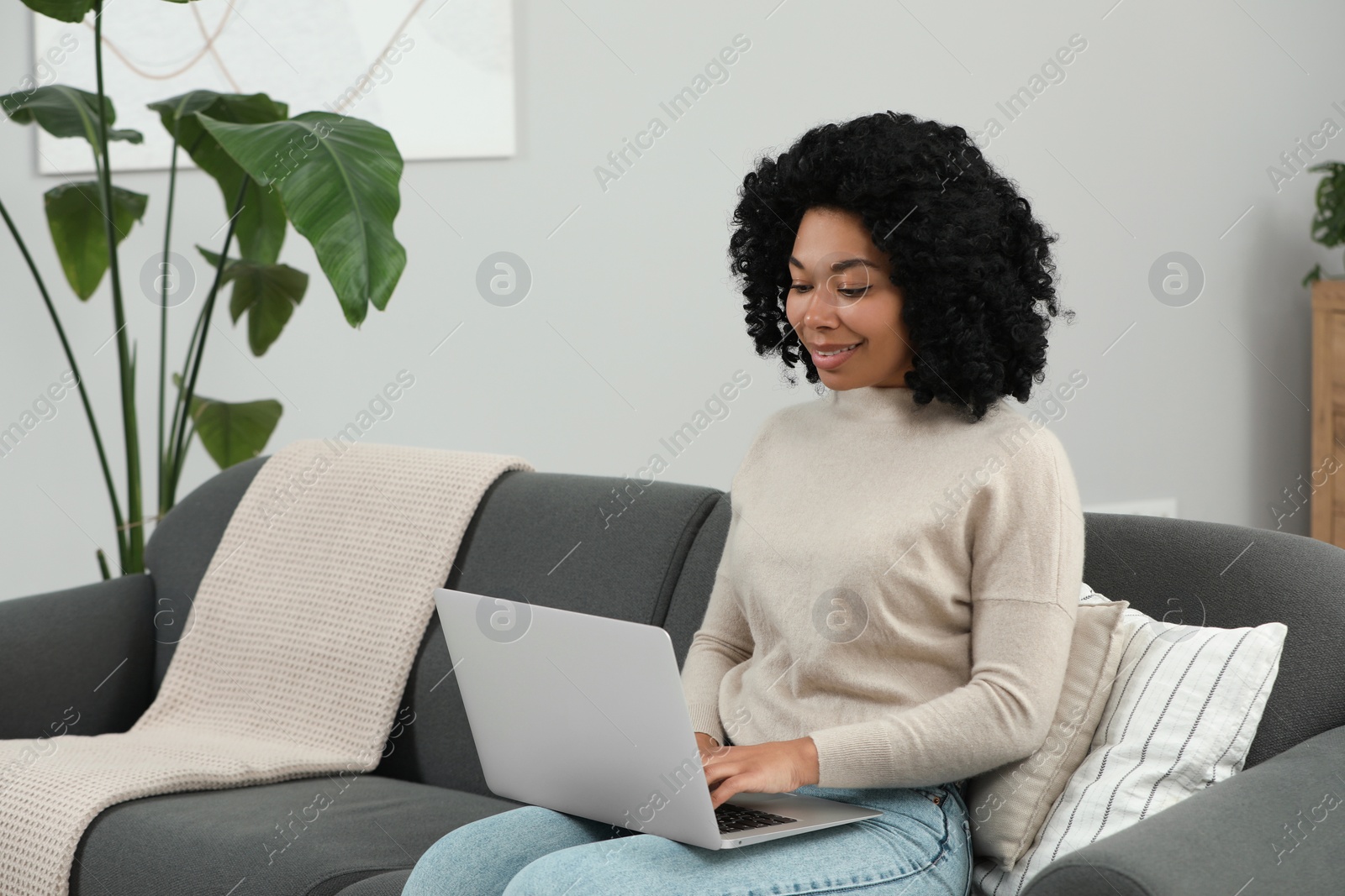 Photo of Happy young woman using laptop on sofa indoors. Space for text