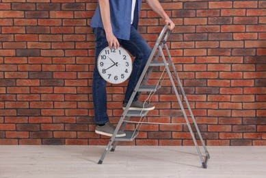 Photo of Man holding clock on stepladder near red brick wall, closeup