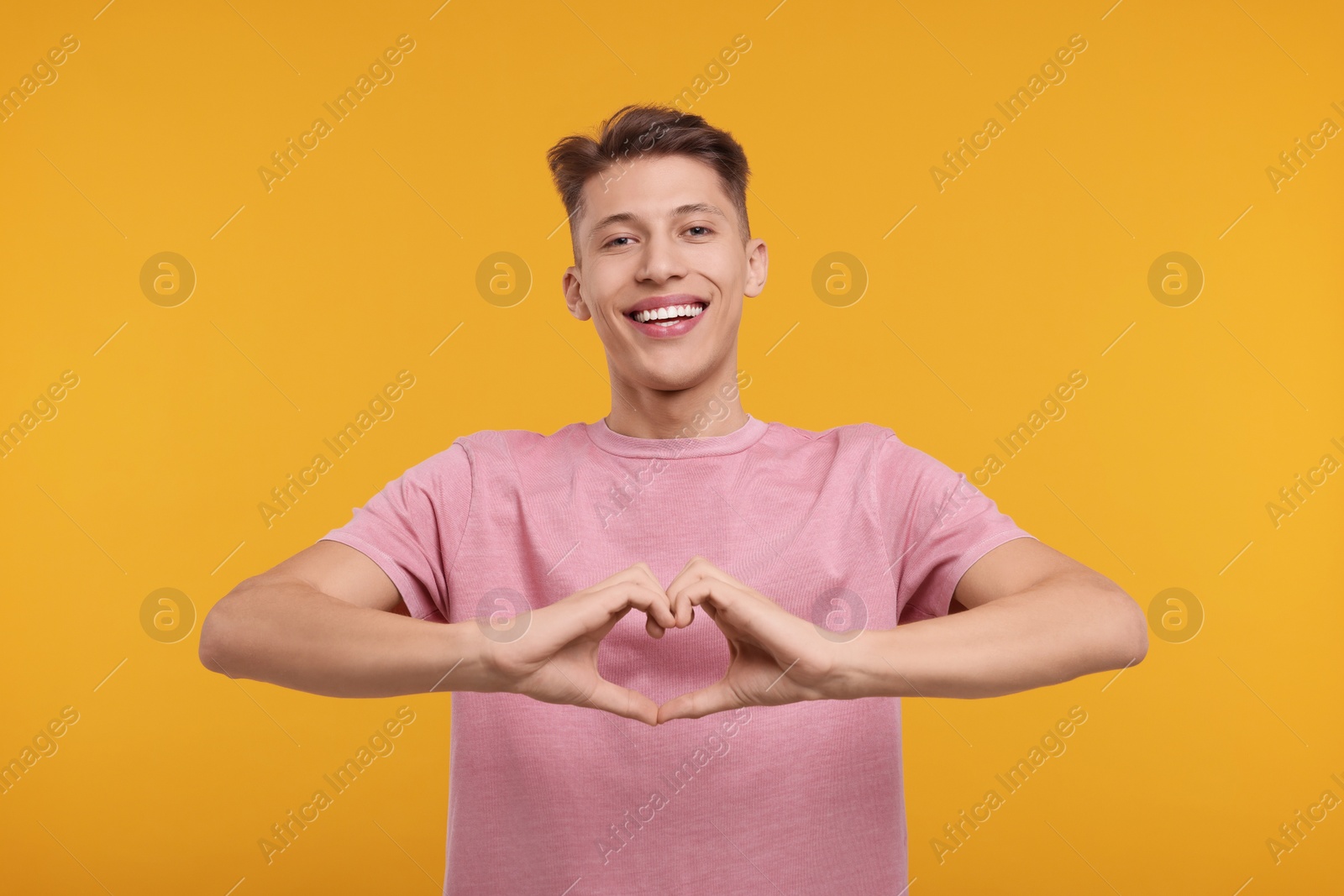 Photo of Happy man showing heart gesture with hands on orange background
